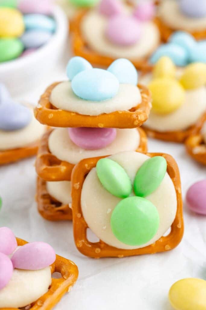bunny shaped pretzels with white chocolate and pastel candies arranged as bunnies, with more treats in the background.