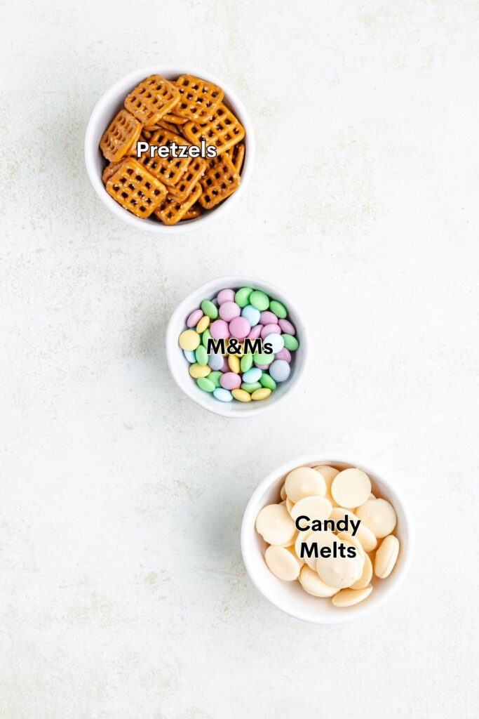 Three bowls with pretzels, pastel M&Ms, and white candy melts, each bowl labeled.