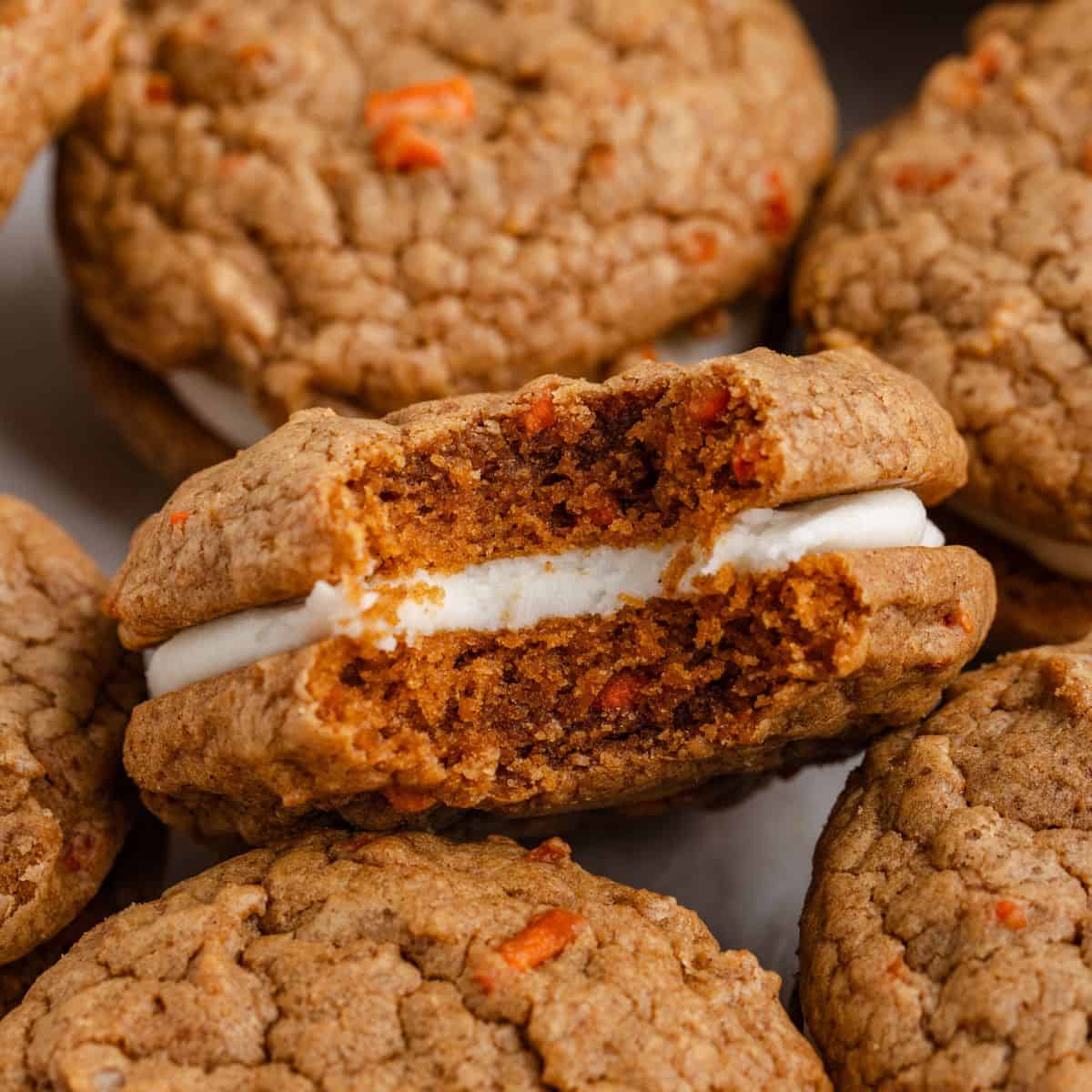 Carrot cake Sandwich cookie with cream cheese filling and a bite taken out, surrounded by other similar cookies, close-up view.