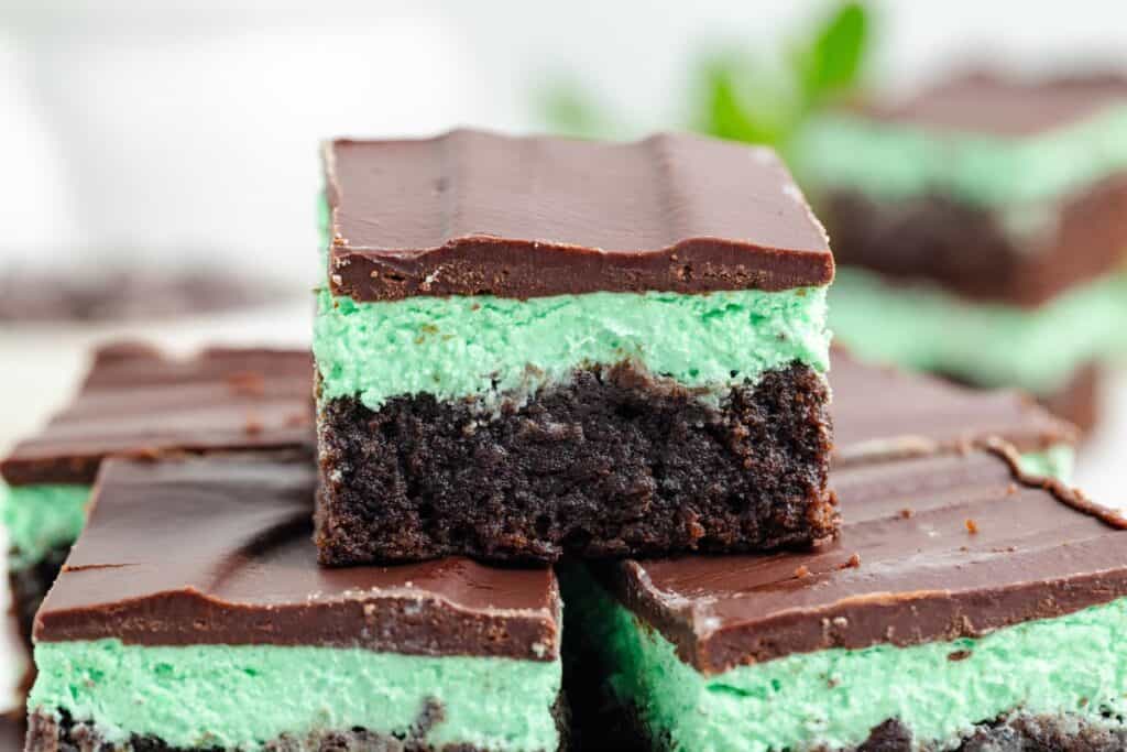 Stacked mint brownies with green mint filling and shiny chocolate topping in a close-up view.