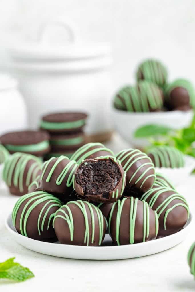 Chocolate mint Oreo truffles with green drizzle on a plate, one bitten to show dark chocolate center; more in the background.