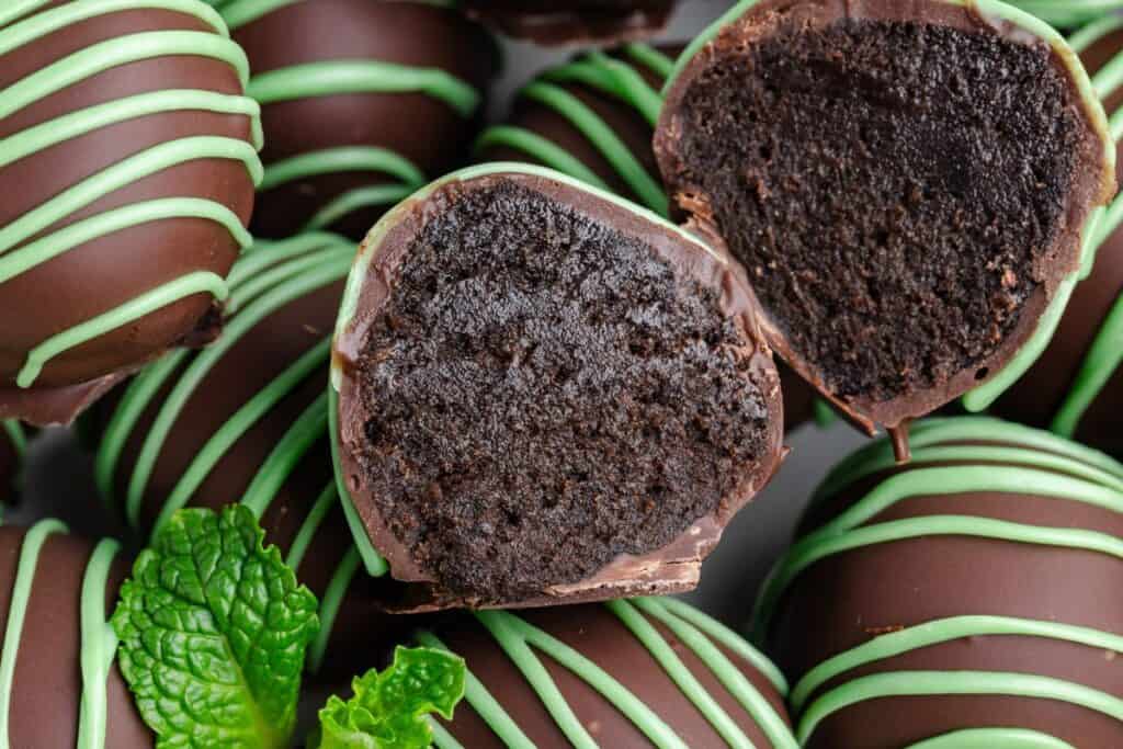 Mint Oreo truffles with green icing, one cut open showing filling, and fresh mint leaves on the side.