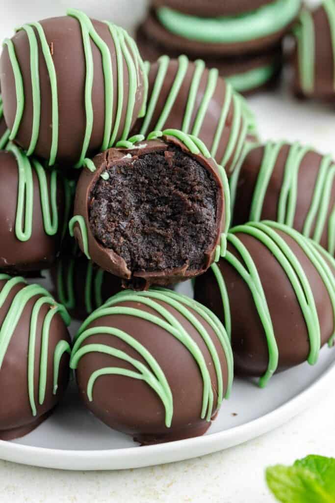 Mint Oreo balls with green icing on a plate; one truffle is bitten, showing its dark fudgy interior.