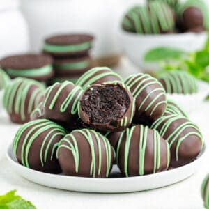 Mint Oreo truffles on a plate, one bitten to show dark filling; cookies sit behind them.