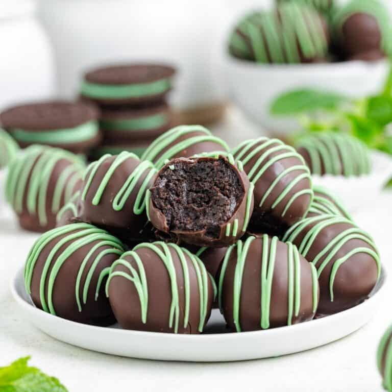 Mint Oreo truffles on a plate, one bitten to show dark filling; cookies sit behind them.