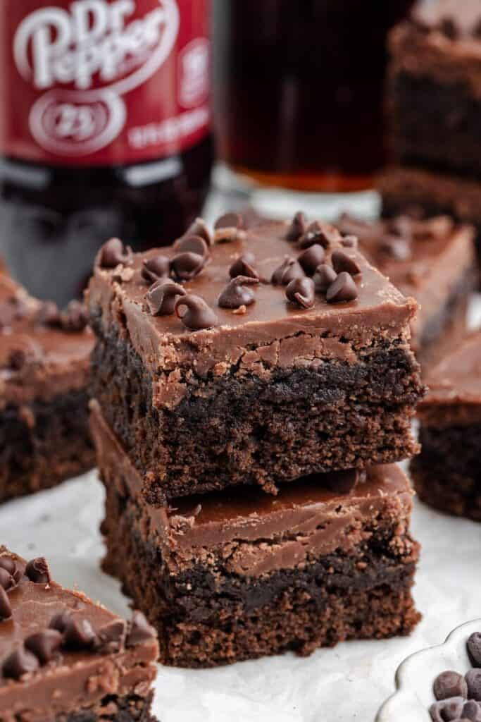 Stack of chocolate Dr Pepper brownies with chocolate chips, Dr Pepper bottle and glass of soda in background.