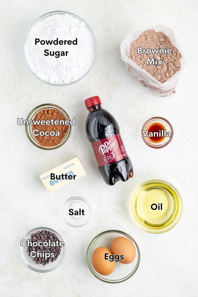 Assorted baking ingredients like brownie mix, cocoa, chocolate chips, and Dr Pepper arranged on a kitchen counter.
