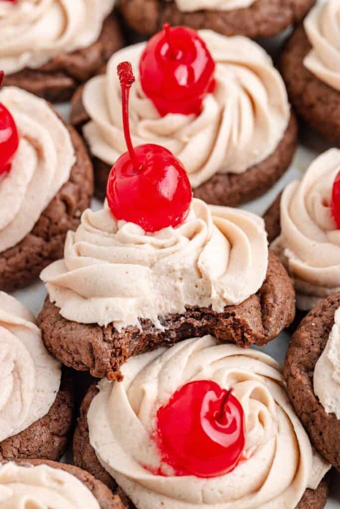 Frosted Dr Pepper  cookies with maraschino cherries, one cookie has a bite taken out.