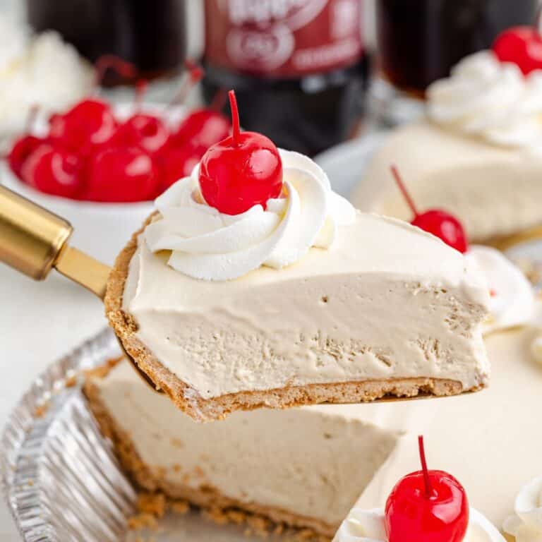 Slice of frozen Dr Pepper pie with graham cracker crust, whipped cream, and cherry being served from a tin.
