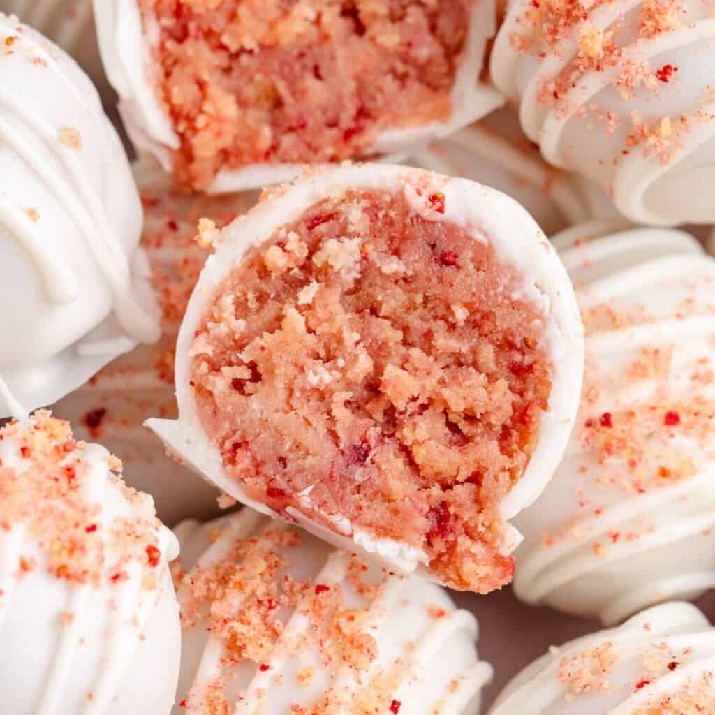 Close-up of white chocolate truffles, one cut open revealing pink strawberry filling, topped with fine crumbs.