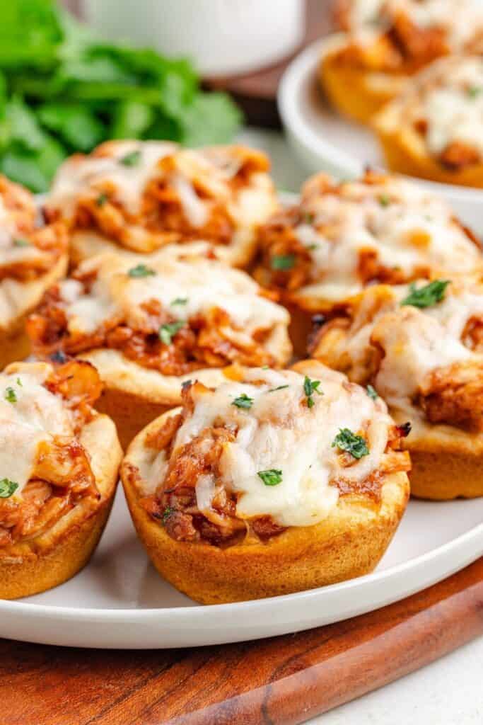 BBQ chicken biscuit cups with shredded chicken, barbecue sauce, melted cheese, and chopped herbs on a plate.