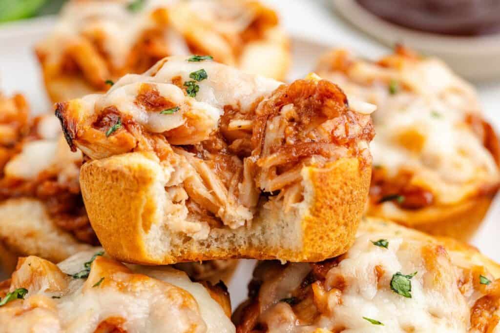 Baked barbecue chicken cups with melted cheese, herbs garnish; one bite taken out.