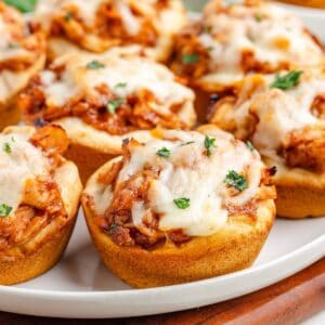 Barbecue chicken biscuit cups with melted cheese and herbs, arranged closely on a white plate.