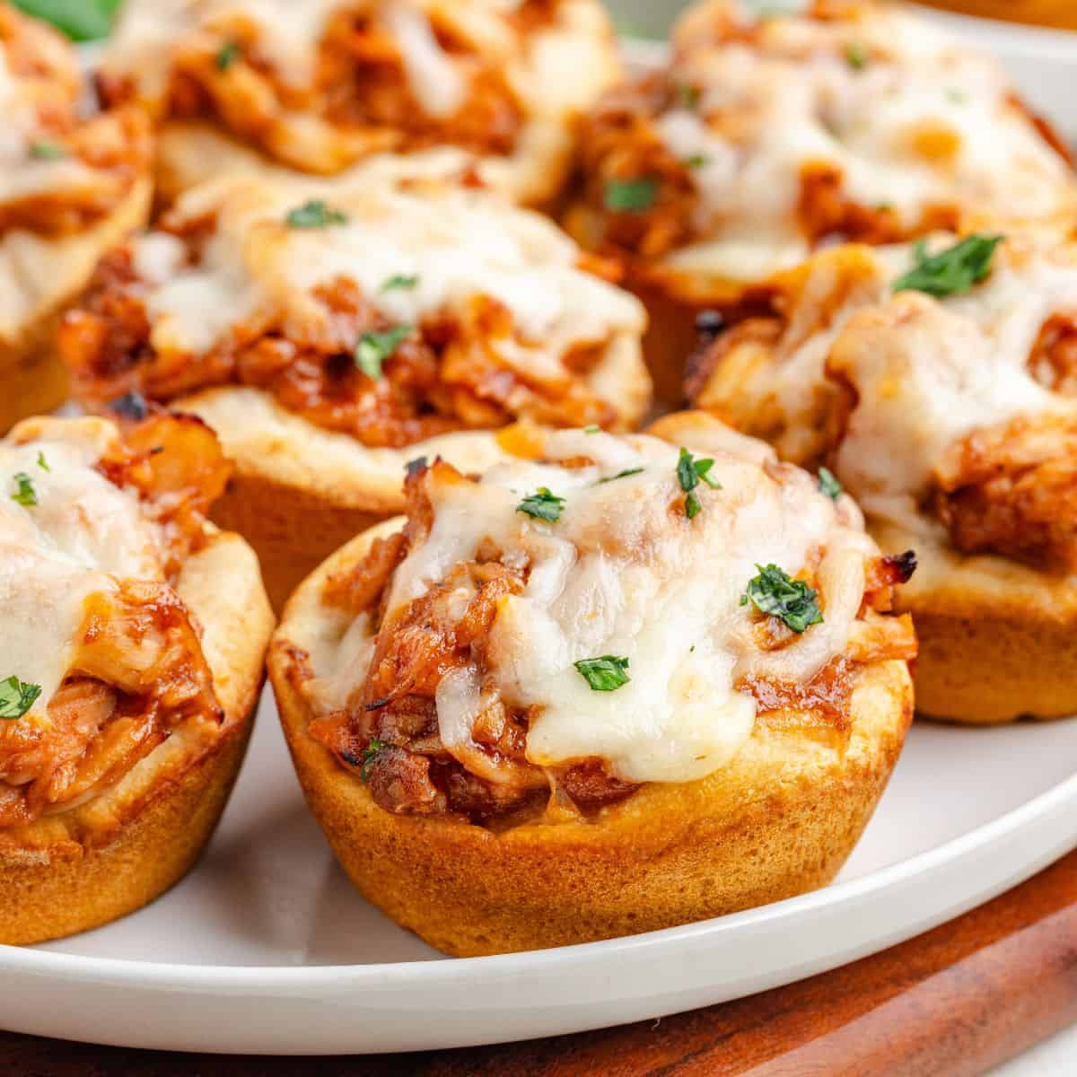Barbecue chicken biscuit cups with melted cheese and herbs, arranged closely on a white plate.