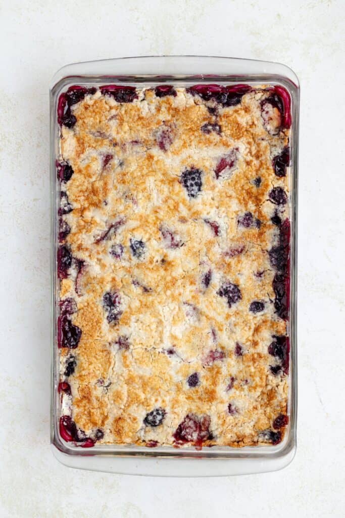 A rectangular glass dish of golden-brown berry cobbler with bubbling fruit and crumbly topping.