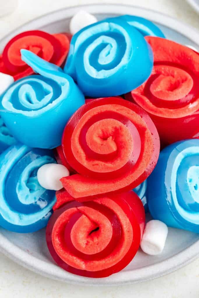 Plate of red and blue spiral jelly roll ups with a few white marshmallows.