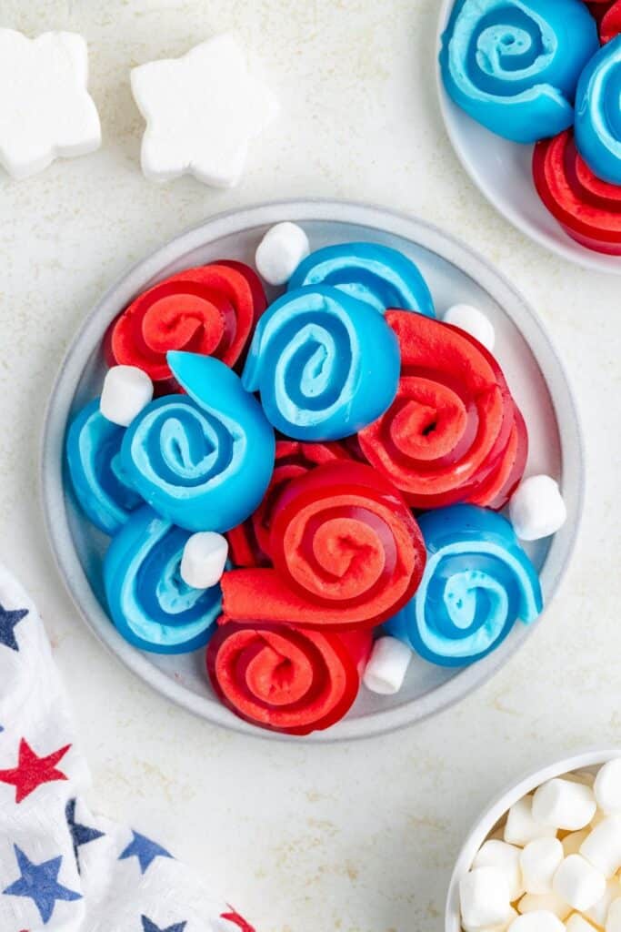 Plate of red and blue spiral gummy candies with mini marshmallows, next to a star-patterned napkin.