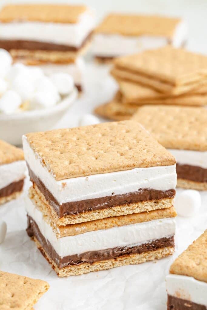 Stack of frozen s'mores with graham cracker, chocolate, and marshmallow layers on parchment, extra bars behind.