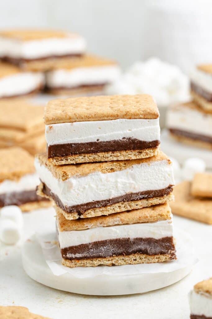 Three s’mores bars stacked on a white plate, displaying graham cracker, chocolate, and marshmallow layers.
