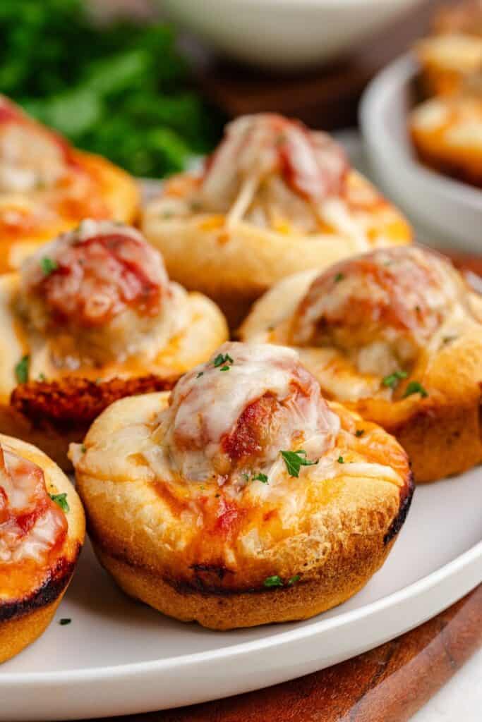 Baked biscuit cups filled with meatballs, tomato sauce, cheese, and herbs on a white plate.