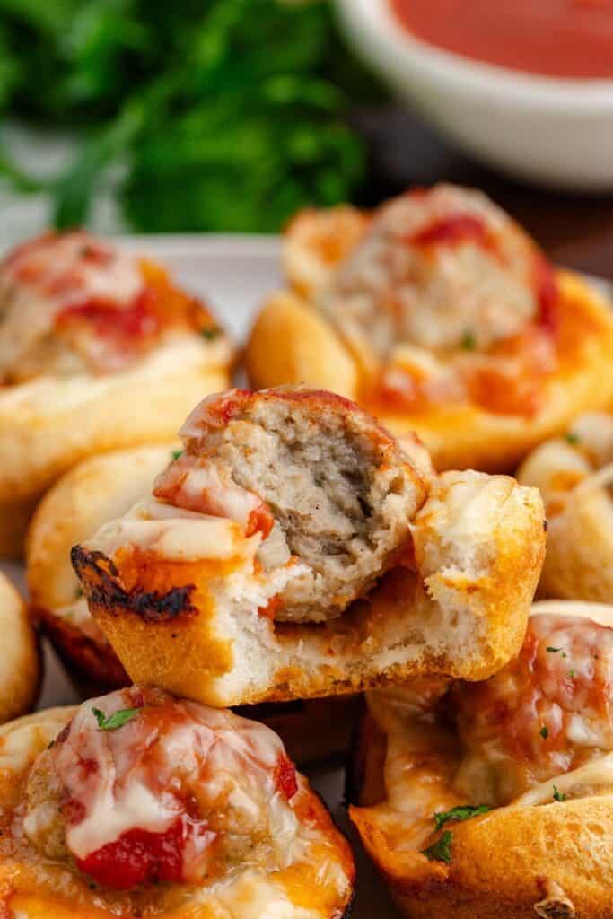 Close-up of meatball sub cupcakes filled with meatballs, cheese, and tomato sauce, one partially eaten.