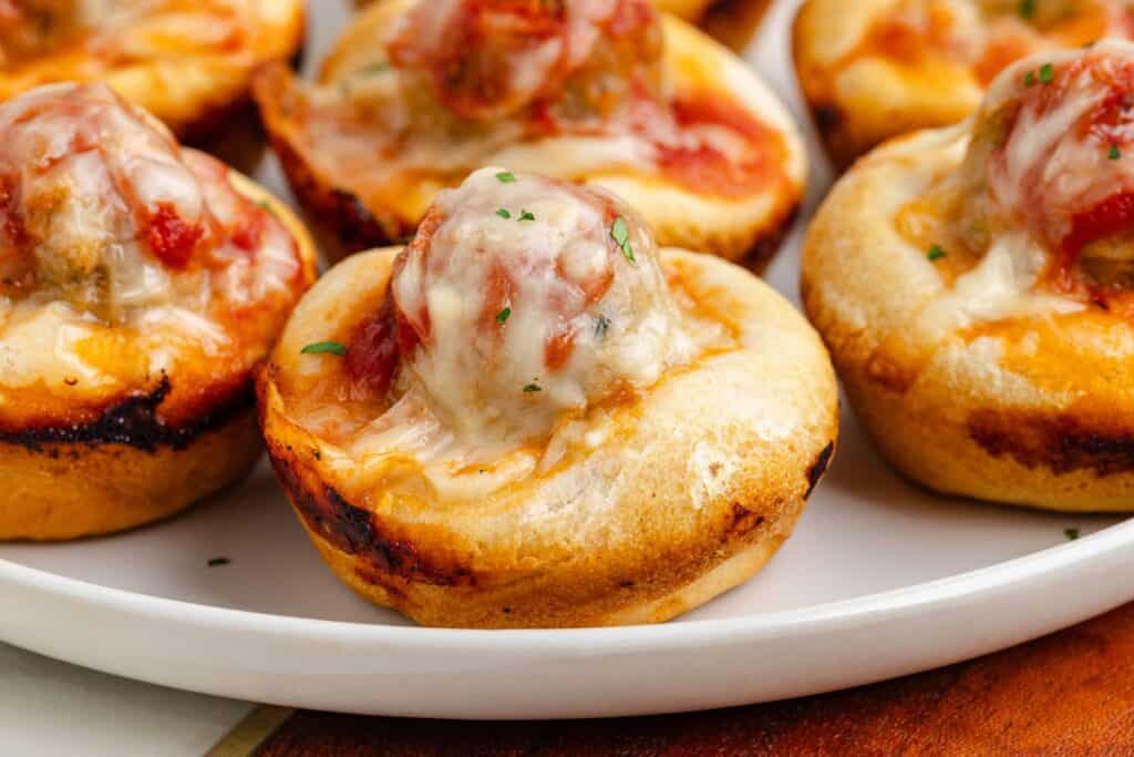Baked Muffin Tin Meatball Subs with meatballs, tomato sauce, and melted cheese on a white plate.