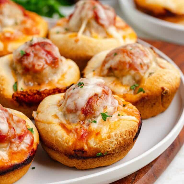 Meatball sub cupcakes with meatballs, melted cheese, and herbs on a white plate.