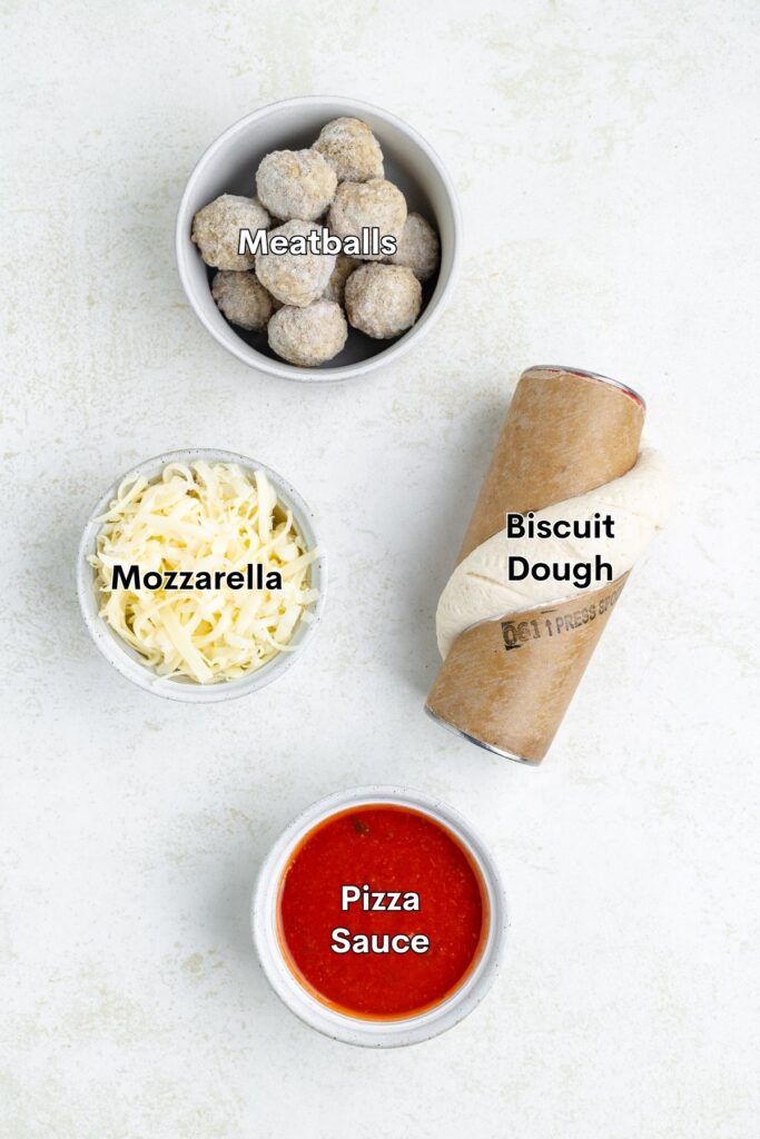 Four labeled ingredients: frozen meatballs, mozzarella cheese, biscuit dough can, and pizza sauce on white surface.