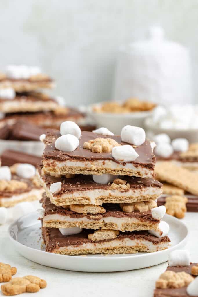 A stack of s'mores bark on a white plate, with extra bars and ingredients nearby.