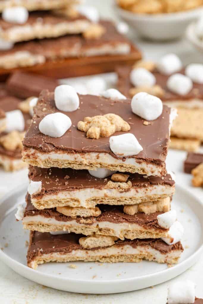 Stack of s'mores bars with chocolate, graham crackers, and marshmallows on a white plate.
