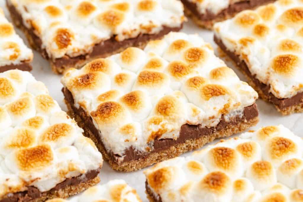 Close-up of smores bars topped with toasted marshmallows, chocolate layer, and graham cracker crust.