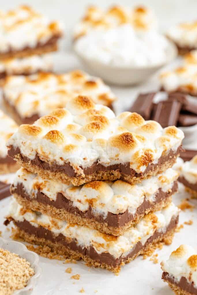 Three stacked s'mores bars with toasted marshmallow and chocolate sit on a graham cracker base.