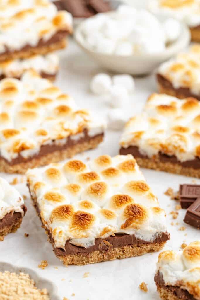 Close-up of smores bars with toasted marshmallow, chocolate, and graham crust on a light surface.