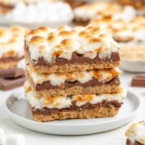 Three stacked s'mores bars with chocolate and toasted marshmallows on a white plate.