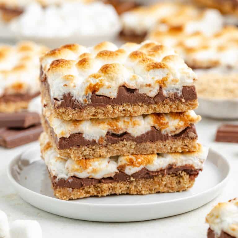 Three stacked s'mores bars with chocolate and toasted marshmallows on a white plate.