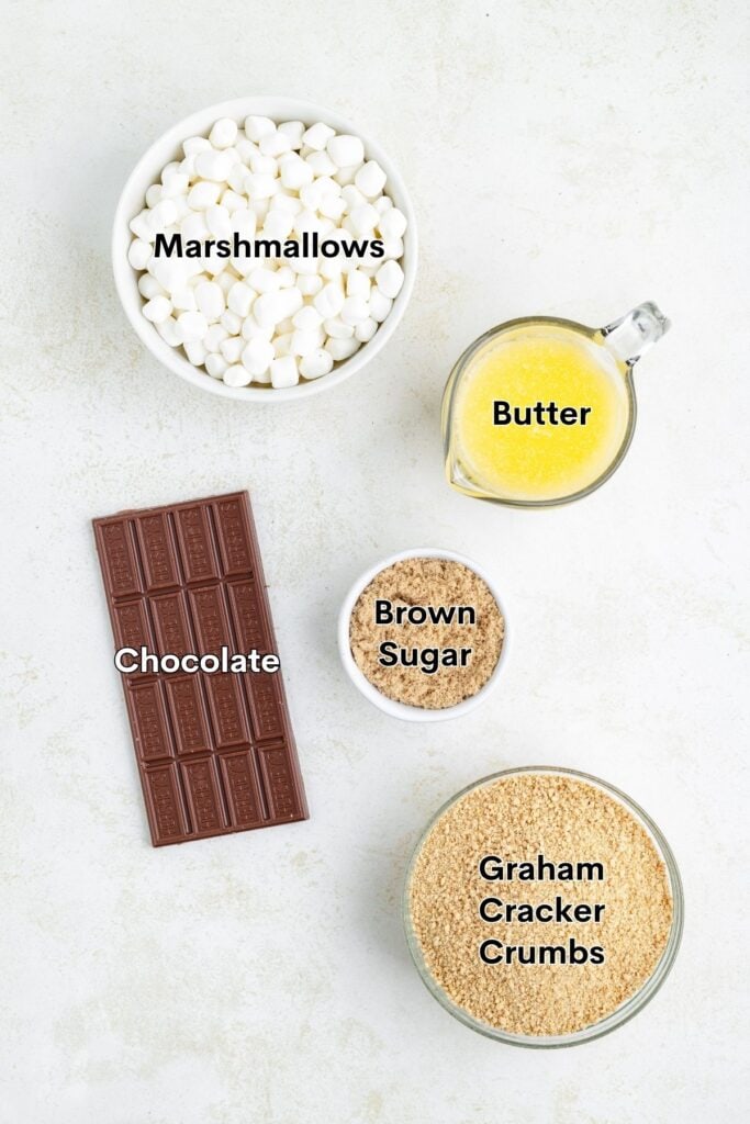 Five labeled ingredients for a recipe: marshmallows, melted butter, brown sugar, chocolate bar, graham cracker crumbs.