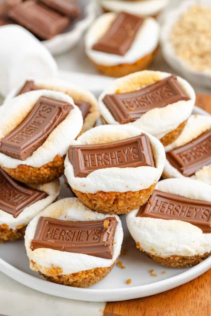 S’mores cups with toasted marshmallow and chocolate pieces on a plate, resting on a wooden surface.