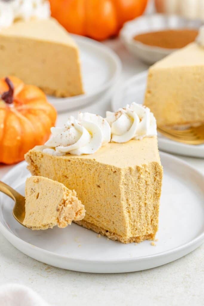 Pumpkin marshmallow pie slice with whipped cream on a white plate, fork holding bite, mini pumpkins behind.