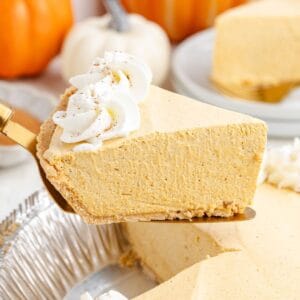 A slice of marshmallow pumpkin pie with whipped cream is lifted from a tin; pumpkins appear in the background.