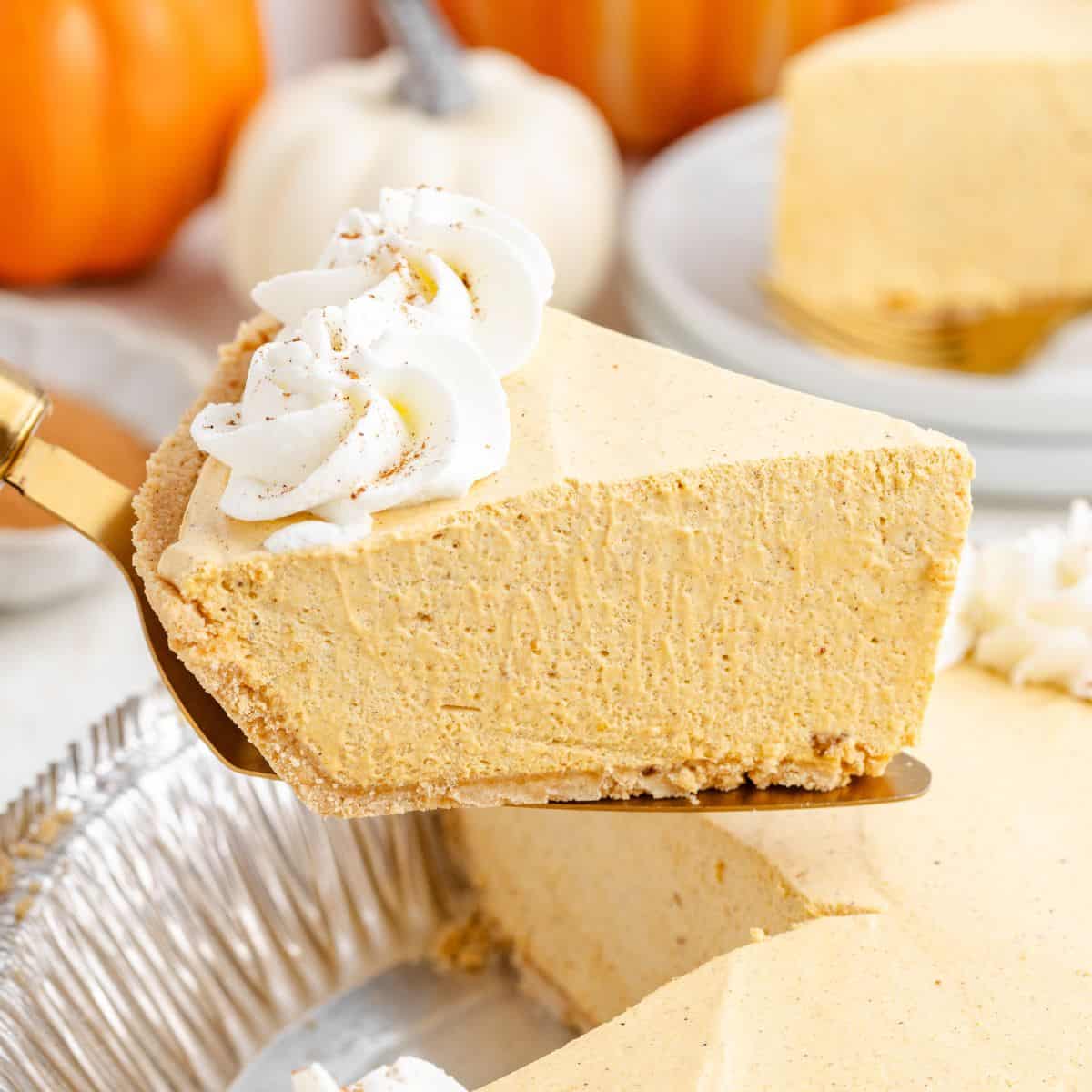 A slice of marshmallow pumpkin pie with whipped cream is lifted from a tin; pumpkins appear in the background.