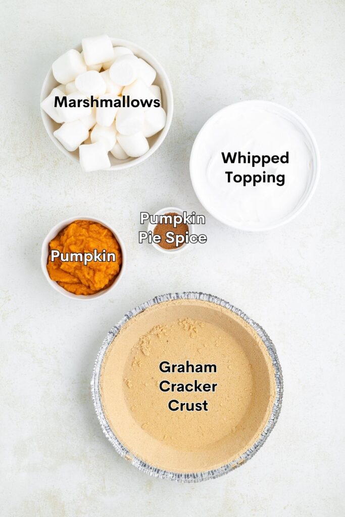 Bowl with marshmallows, whipped topping, pumpkin, spice, and graham crust on a light surface.