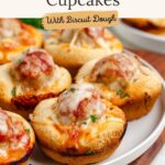 Plate of biscuit dough cupcakes with meatball filling, tomato sauce, cheese, and herbs. Text: Meatball Sub Cupcakes.