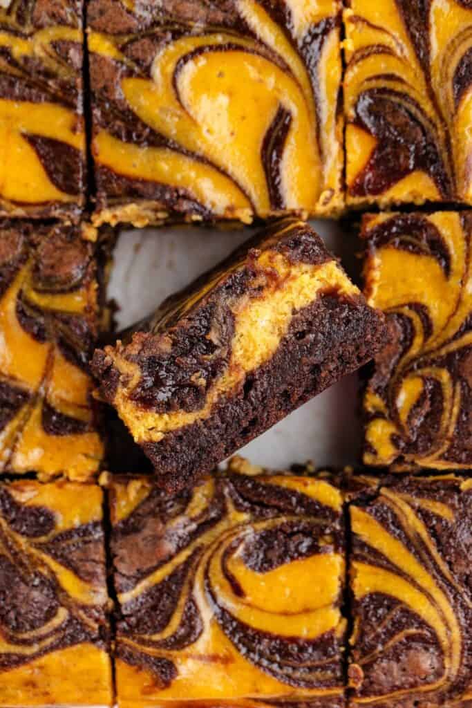 Pumpkin chocolate brownies cut into squares, one square lifted to display marbled layers.