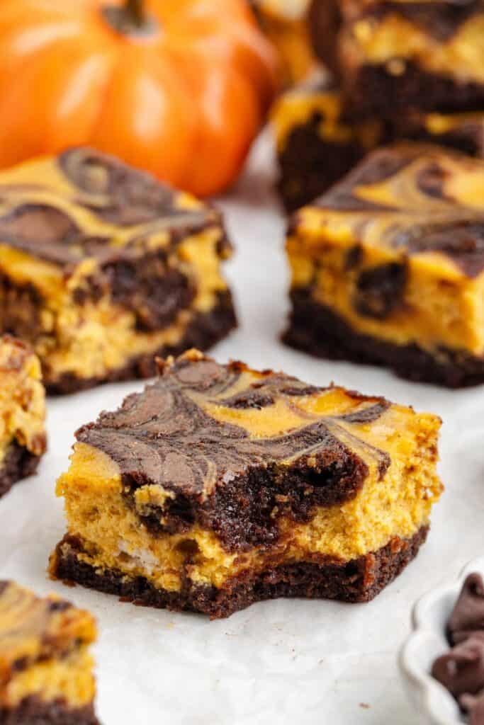 Close-up of swirled pumpkin cheesecake brownies with orange and chocolate layers on a white surface.