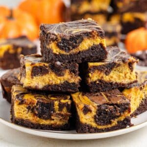 Plate of pumpkin cheesecake brownies, with blurred small pumpkins in the background.