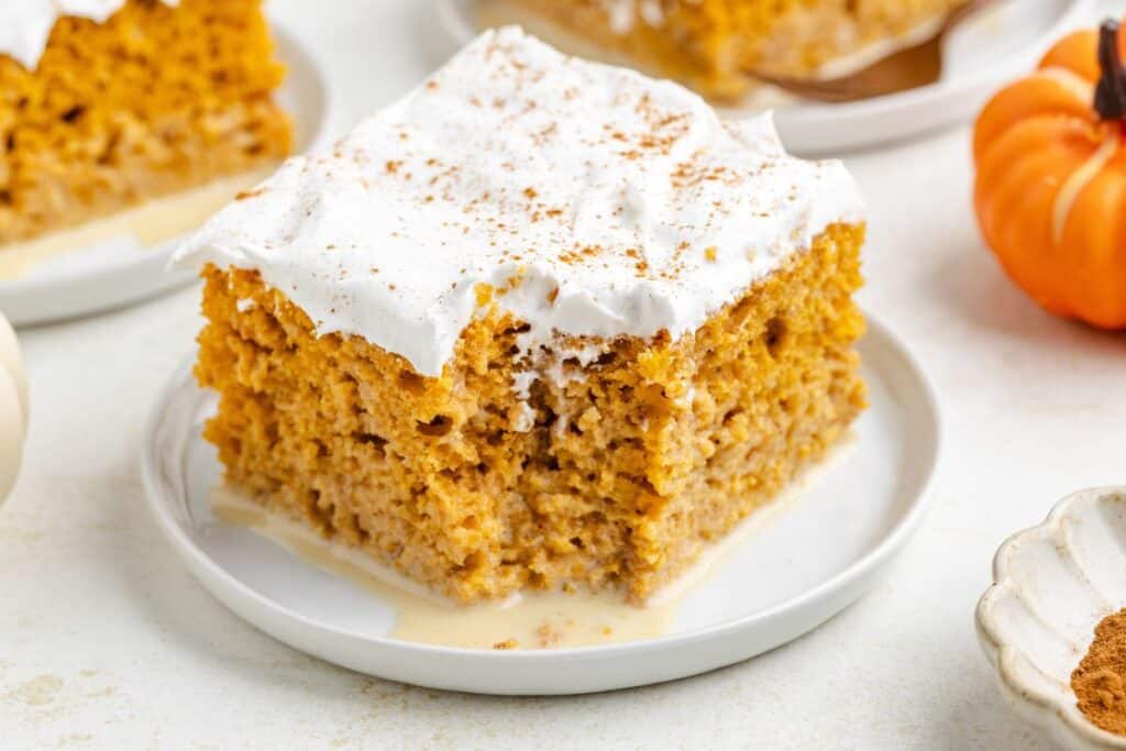 Pumpkin tres leches cake slice with whipped topping and cinnamon on top, served on a white plate.