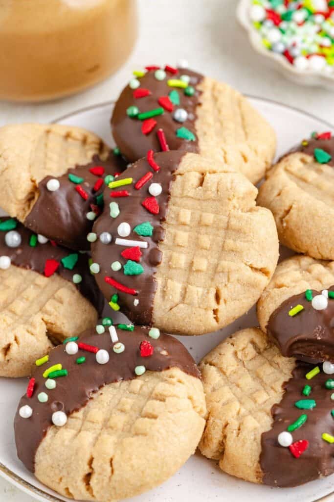 Peanut butter chocolate dipped cookies with holiday sprinkles on a white plate.