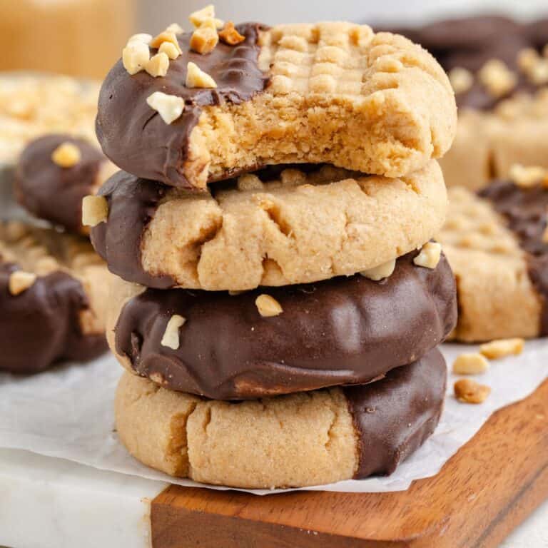 Stacked chocolate dipped peanut butter cookies with chopped nuts and a bite taken from the top.