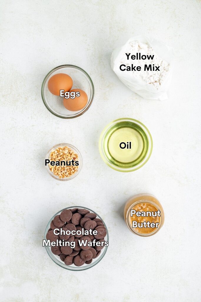 Six labeled baking ingredients arranged separately on a light surface: cake mix, eggs, oil, peanuts, peanut butter, chocolate wafers.