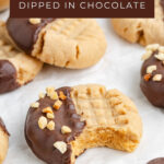 Chocolate-dipped peanut butter cookies with chopped nuts on parchment, one featuring a bite taken out.